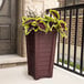 A Mayne cranberry red planter with a potted plant on a porch.