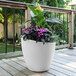 A Mayne Modesto white planter with a potted plant with pink flowers.