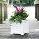 A white Mayne Lakeland planter with pink flowers on a wooden deck.