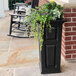 A black Mayne Nantucket planter with flowers in it on an outdoor patio.