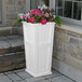 A Mayne white planter with pink flowers on top sitting on steps.
