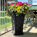 A black Mayne Georgian rectangular planter with colorful flowers on an outdoor patio table.