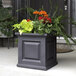A square graphite gray Mayne planter with flowers and ferns on an outdoor patio table.