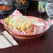 A red round deli server holding tacos on a table.