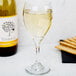 A Libbey white wine glass filled with white wine next to a bottle of wine and crackers.