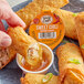 A hand dipping a Sauce Craft Sweet Chili Sauce into a fried egg roll.