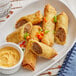 A white plate with The Gourmet Egg Roll Co. Philly Cheesesteak Egg Rolls and dipping sauce.