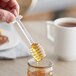 A hand using an Acopa plastic honey dipper to drizzle honey into a jar.
