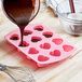 A pink Wilton heart-shaped silicone mold with liquid being poured into it.