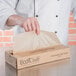 A hand opening a brown box of Bagcraft Packaging EcoCraft deli wrap.