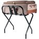 A black Lancaster Table & Seating folding luggage rack holding a luggage bag.