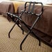 A black metal Lancaster Table & Seating folding luggage rack with straps.
