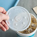 A hand holding a Dart translucent plastic lid with a straw slot over a plastic cup filled with ice and soda.