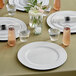 A table set with white Choice beaded rim charger plates, glasses, and vases.