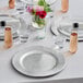 A table set with Choice silver charger plates, glasses, and flowers.