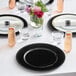 A table set with black Choice beaded rim charger plates, glasses, and pink flowers.
