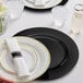 A white table with Choice black plastic charger plates on white plates with a white napkin.