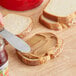 A person spreading Jif Creamy Peanut Butter on a slice of bread with a knife.