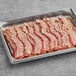 A tray of Swift Fully Cooked thick bacon slices on a gray surface.