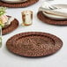 A table set with an Acopa Brunet rattan charger plate, utensils, and a brown woven placemat.