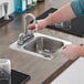 A person washing their hands in a Regency stainless steel drop-in sink with a gooseneck faucet.