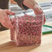 A person holding a Cambro square polycarbonate food storage container full of pink round candies.