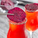 Two glasses of red and purple drinks garnished with dried red dragon fruit slices.