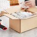 A hand using a box cutter to open a Lavex Kraft cardboard shipping box.