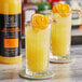 Two glasses of Twisted Alchemy Valencia Orange Juice with orange slices on top.