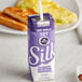 A purple carton of Silk Very Vanilla soy milk on a table with food.