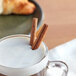 A glass mug of milk with McCormick Culinary Cinnamon Sticks on top.