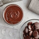 A bowl of Republica del Cacao dark chocolate couverture and a whisk on a counter.