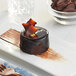 A chocolate cake on a plate with a piece of Valrhona dark chocolate on top.