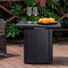 A black stainless steel square fire pit table with a plate of oranges and wine glasses on it.