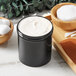 A black plastic jar filled with white cream next to a wooden bowl of cotton pads.