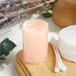 A Clear Regular Wall Polystyrene Jar filled with pink liquid on a wooden surface.