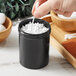 A hand holding a black container filled with white cotton balls.