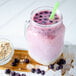 A pink smoothie with blueberries in a glass jar with a straw on the side.