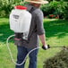 A man using a Chapin battery-powered backpack sprayer to spray a bush.