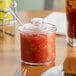 A clear Choice plastic condiment jar with red sauce and a spoon on a table.