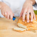 A person using a blue Mercer Culinary bread knife to cut a loaf of bread.