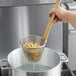 A person using a Thunder Group fine mesh noodle skimmer with a bamboo handle to strain pasta.