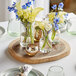 An Acopa round acacia wood serving board on a table with vases of flowers.