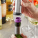 A hand using a silver and purple Acopa wine saver to seal a bottle of wine.