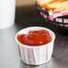 A Solo white paper souffle cup filled with ketchup next to a basket of french fries.