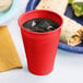 A Classic Red Plastic cup with ice in it next to a plate of food.