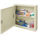 A beige Omnimed wall-mount medical storage cabinet with many boxes and other items inside.