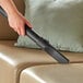A person using a Lavex Pro wet/dry vacuum to clean a couch.