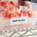 A plastic container of orange Regency label holders with ear plugs inside.