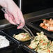 A hand using a Cambro clear plastic salad bar spoon to serve food from a tray.